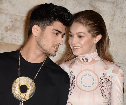 Couple smiling at each other, the man wears a pendant and the woman is in a patterned outfit; close-up.