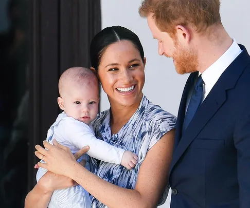 Smiling woman holds a baby while standing next to a man in a suit.