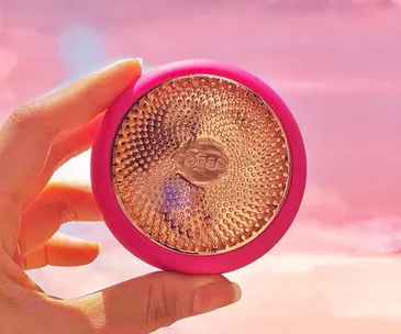 Hand holding a pink FOREO UFO device against a pink sky background.