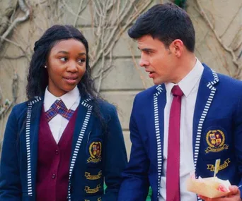 Two students in blue school uniforms are walking and talking outside.