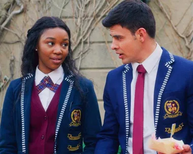 Two students in blue school uniforms are walking and talking outside.