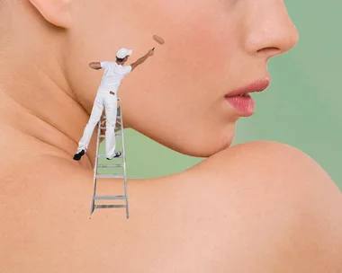 A tiny painter stands on a ladder applying makeup to a large woman's cheek, demonstrating creative pimple coverage.