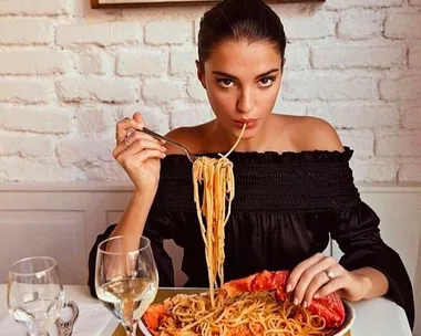 Woman in a black top eating spaghetti and lobster at a restaurant with white brick walls.