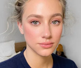 Portrait of a young woman with blonde hair, green eyes, and natural makeup, wearing a dark navy blue top.