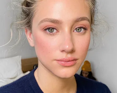 Portrait of a young woman with blonde hair, green eyes, and natural makeup, wearing a dark navy blue top.