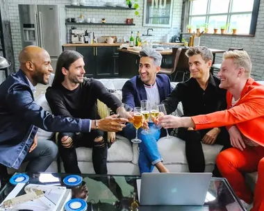 Five people sitting on a couch in a kitchen, clinking glasses and smiling, in a bright and modern setting.