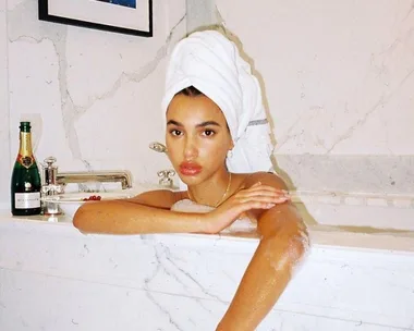 Woman in a marble bath with a towel on her head, champagne bottle on the tub edge.