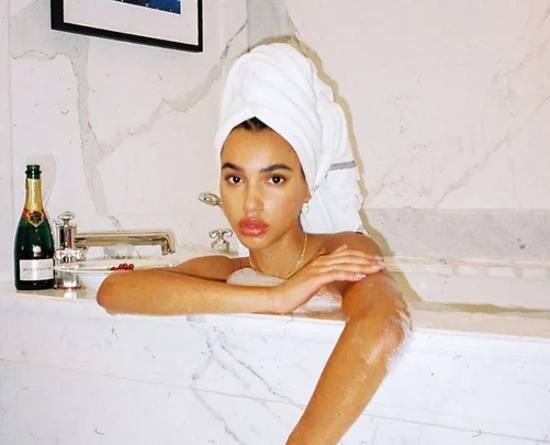 Woman in a marble bath with a towel on her head, champagne bottle on the tub edge.