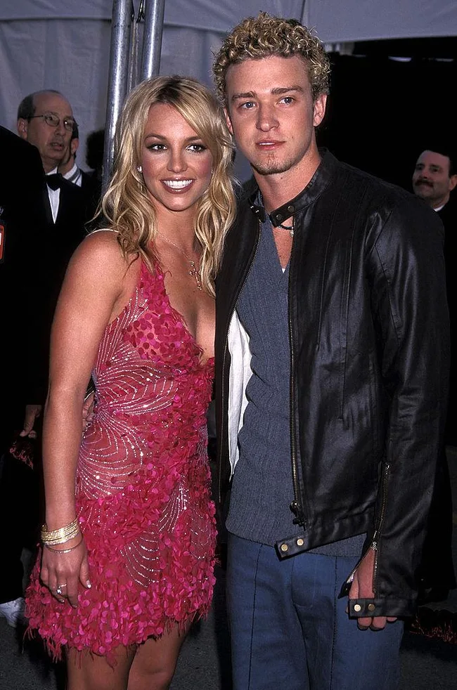 A woman in a pink dress and a man in a leather jacket smile together at an event.