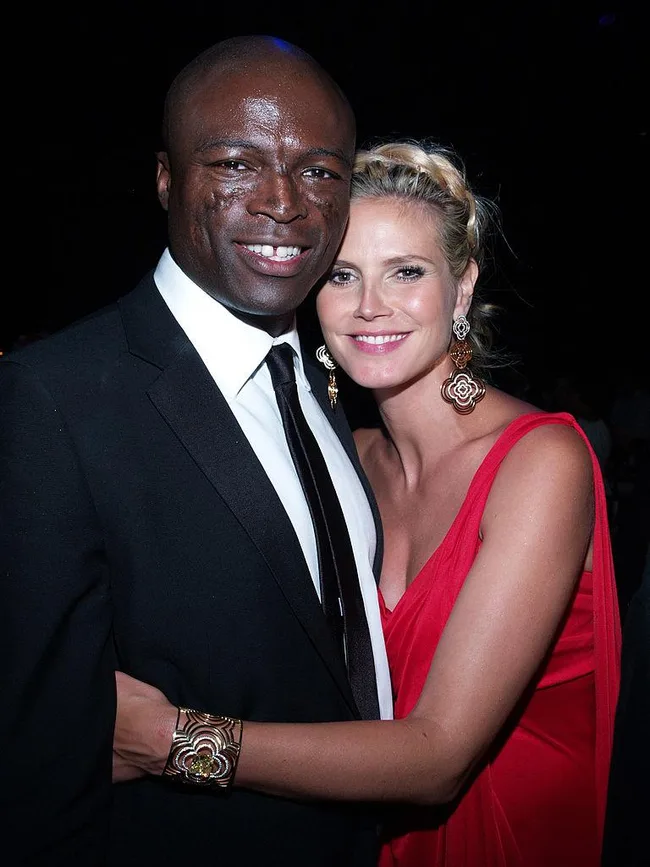 Man in a black suit and woman in a red dress smiling and embracing at a formal event.