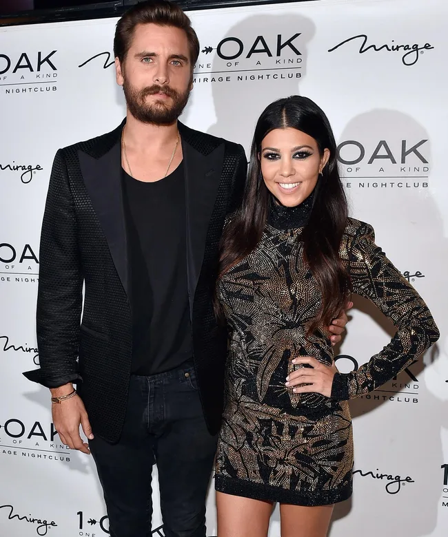 Man in a black jacket and woman in a patterned dress pose at the 1 OAK Nightclub event at Mirage, with logos behind them.