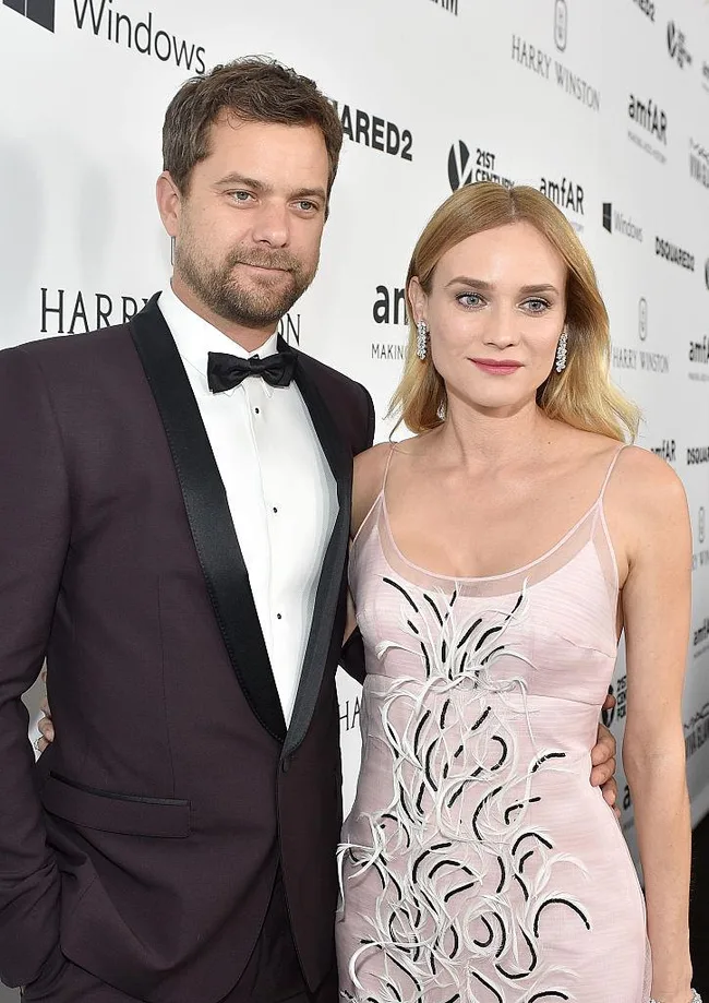 Two people at an amfAR event, one in a dark suit, the other in a light floral dress, both posing for photos.