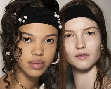 Two models wearing black headbands with pearls, showcasing natural makeup with gold eyeliner.