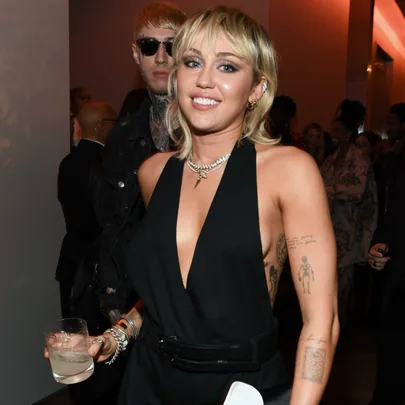 A woman with short hair in a black outfit holding a drink at a crowded event.