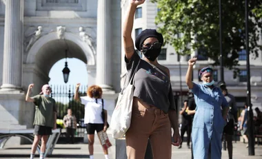 Protesters wearing masks raise fists during a Black Lives Matter demonstration in front of an arch.