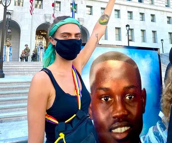 A protester with a raised fist wears a mask and stands by a photo of Ahmaud Arbery during a Black Lives Matter protest.