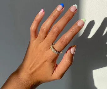 A hand with rainbow-colored French tips on nails and a sparkling ring on the finger.