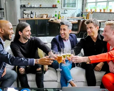 The "Queer Eye" cast toasting with drinks on a modern kitchen set.