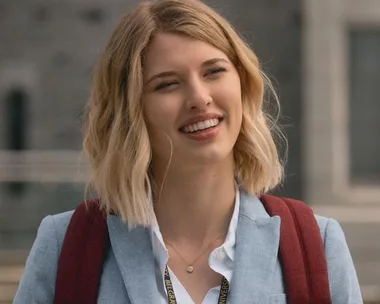 Woman with short blonde hair wearing a blue blazer and red backpack, outdoors, smiling.