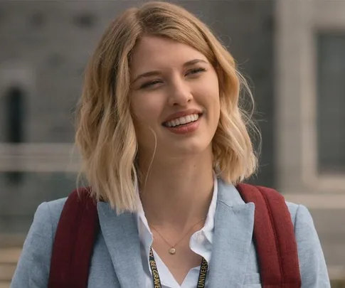 Woman with short blonde hair wearing a blue blazer and red backpack, outdoors, smiling.