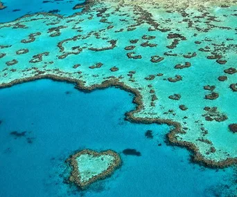 Aerial view of the Great Barrier Reef with a heart-shaped coral formation in turquoise water.