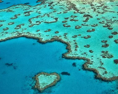 Aerial view of the Great Barrier Reef with a heart-shaped coral formation in turquoise water.