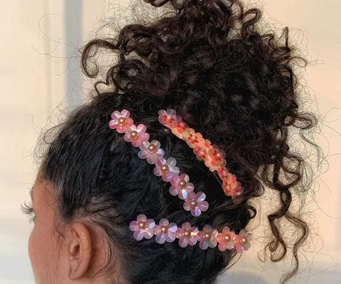 Curly hair styled with colorful flower hair clips on the side.