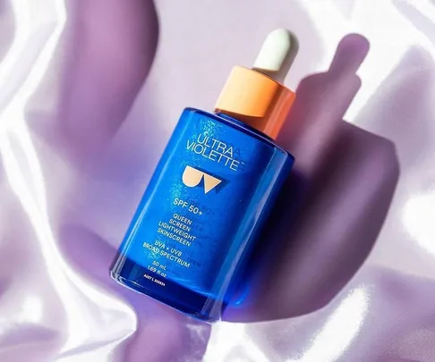 Blue bottle of Ultra Violette sunscreen with dropper cap, SPF 50+, on silky lilac background.