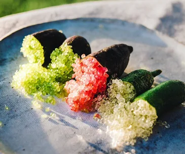 A plate with finger limes, cut open to reveal green, pink, and translucent citrus pearls spilling out.