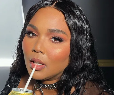 Woman with long, wavy hair and makeup, sipping a drink through a straw, wearing a choker necklace.