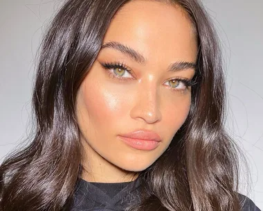 A woman with glowing skin and glossy, wavy hair in a close-up portrait.