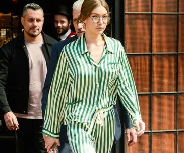 Woman in green striped pajamas walking on the street with glasses, surrounded by several people in the background.