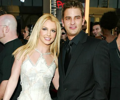 Two people smiling at a public event, with the woman in a white dress and the man in a black suit.