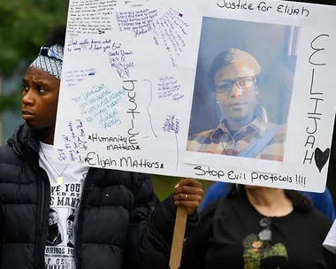 A protester holds a sign with messages and a photo of Elijah McClain, demanding justice and change.