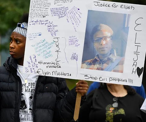 A protester holds a sign with messages and a photo of Elijah McClain, demanding justice and change.