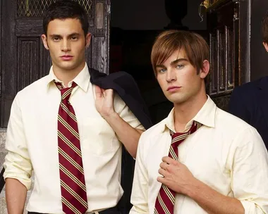 Two young men in school uniforms with striped ties stand outside a building, one holding a jacket over his shoulder.