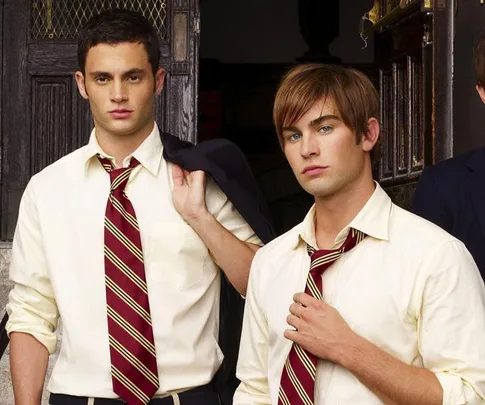 Two young men in school uniforms with striped ties stand outside a building, one holding a jacket over his shoulder.