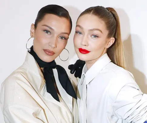 Two women in stylish outfits pose together, with one wearing hoop earrings and the other with bright red lipstick.