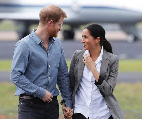 A smiling couple, holding hands, disembarks from a private jet, with an airfield in the background.