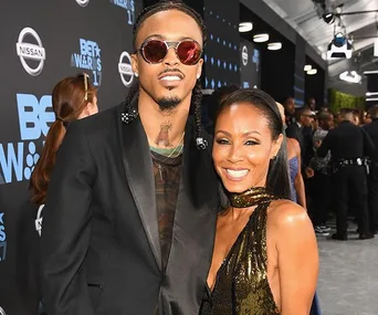 A man in a black suit and sunglasses poses with a woman in a gold dress on the red carpet at the BET Awards event.