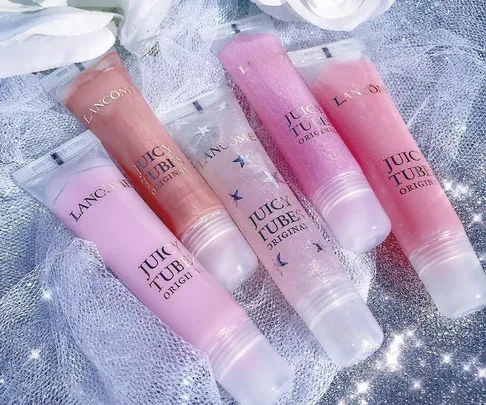 Five Lancome Juicy Tubes lip glosses in shades of pink and peach on sparkly fabric.