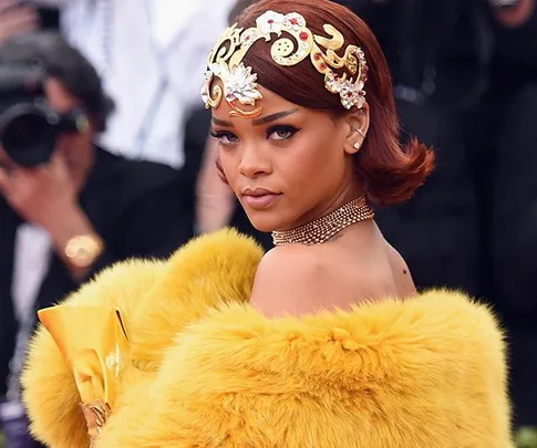 Rihanna at the 2015 Met Gala wearing a yellow fur gown and ornate headpiece, posing elegantly on the red carpet.