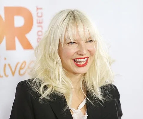 Singer Sia smiling at a public event with a white backdrop.