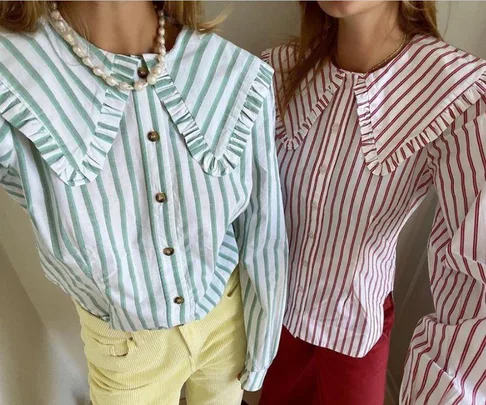 Two women wearing striped shirts with oversized ruffled collars, one in green and the other in red.