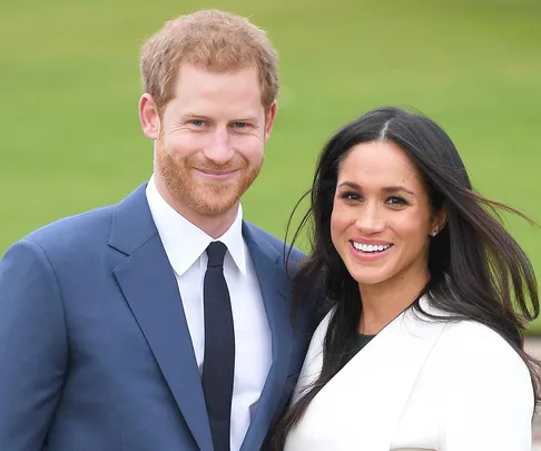 A smiling couple outdoors, woman in white coat, man in blue suit and tie.