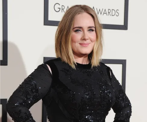 A woman in a black sequined dress poses confidently at a formal event with award logos in the background.