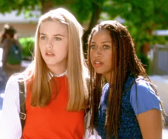 Two teenage girls from "Clueless" look surprised outdoors; one wears a red sweater, and the other a blue top.