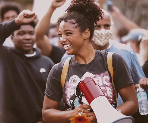 Protester holding a megaphone smiles amidst a crowd with raised fists during a demonstration.