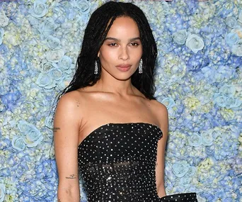 Person in a strapless black dress with silver studs in front of a wall of blue and white flowers.