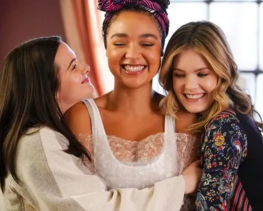 Three women smiling and embracing in a warm hug, highlighting friendship and joy.